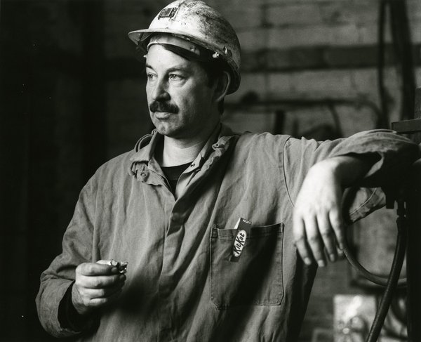 Black and white image of a coal miner eating a Kit Kat biscuit. He is wearing his helmet