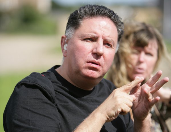 A man wearing a hearing aid is using sign language to communicate with another person