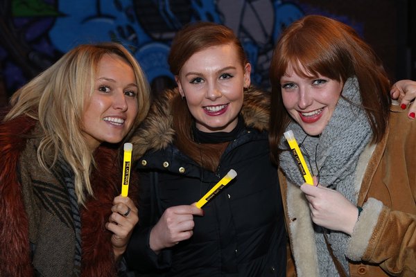  Three woman smile towards the camera while holding yellow glow sticks at The Late Shows event in 2015