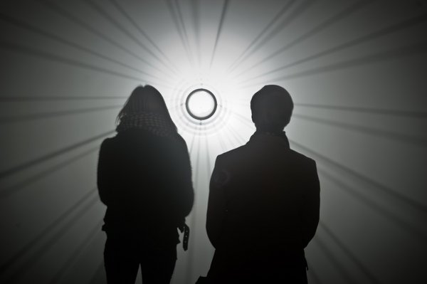  A man and woman in silhouette look towards an art installation featuring a bright, white circular light