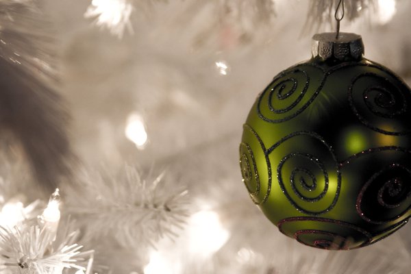 Close-up of a green bauble on a white artificial Christmas tree with fairy lights